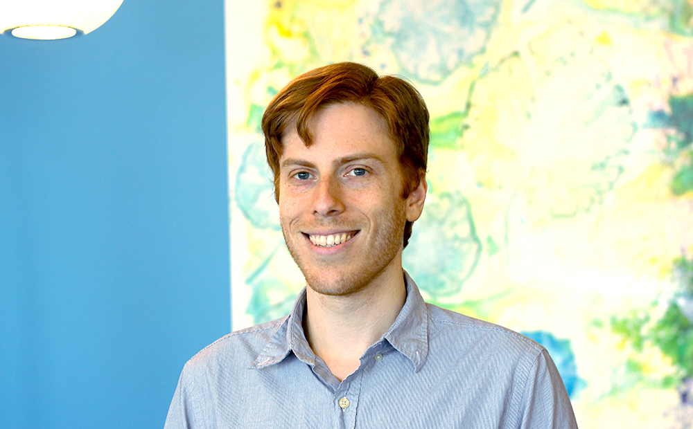 Lewis in a collared shirt in front of office artwork