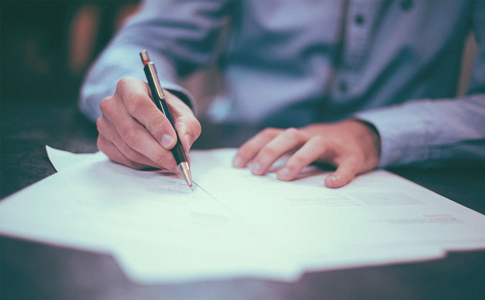 Man in collared shirt reviewing documents with a pencil.