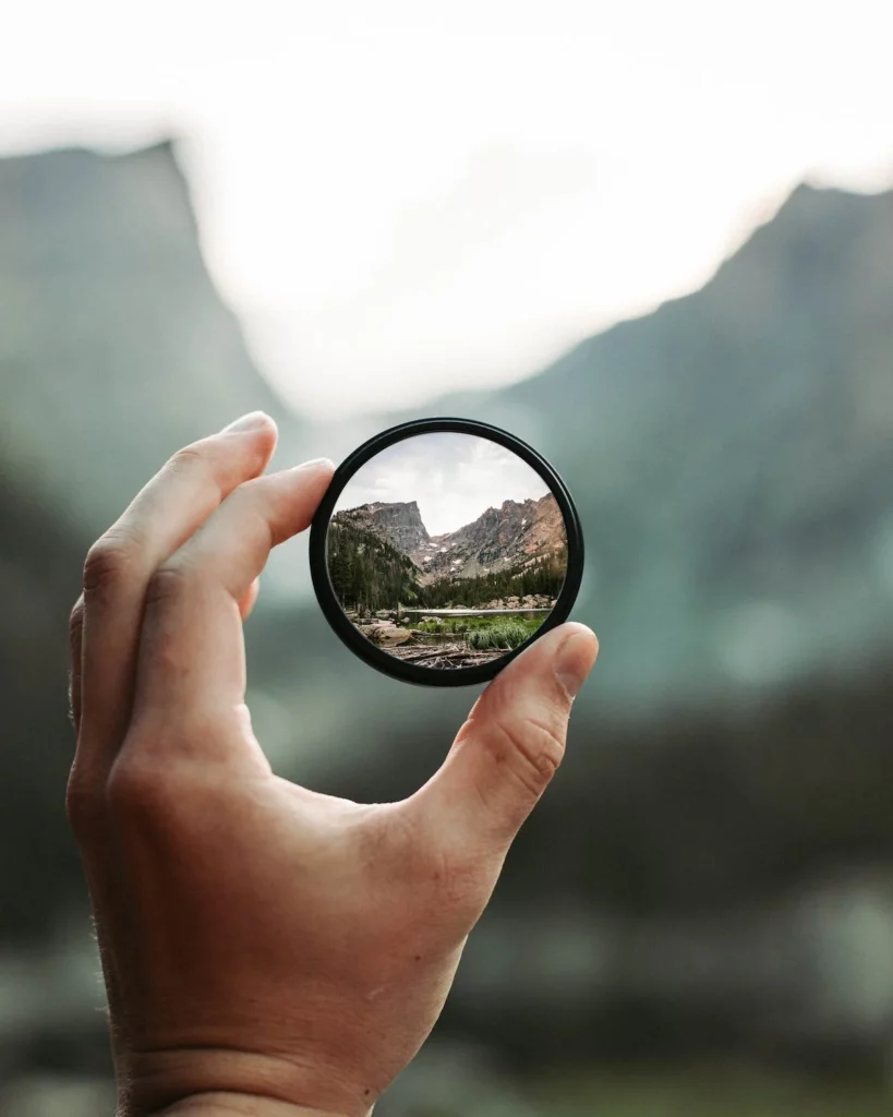 A hand holding a glass ring. The background is blurry, except for the circle visible through the ring which is a clearly visible mountain. 