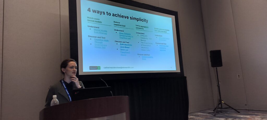 Catherine standing under a projection of a slide that reads "4 ways to achieve simplicity".