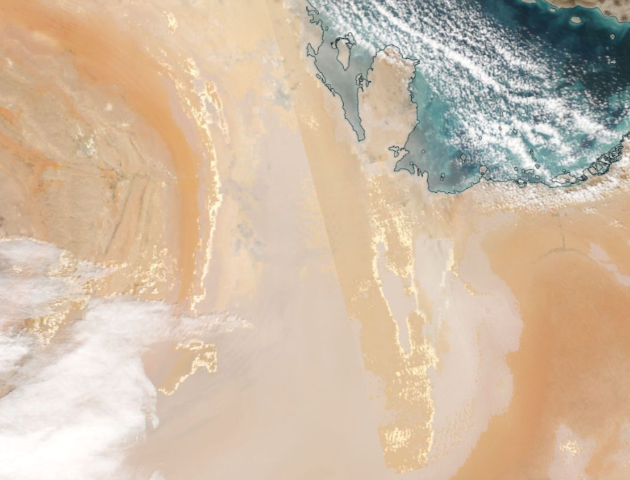 Aerial image demonstrating normal reflectance in dust visibility. Clouds and a body of water are visible. 