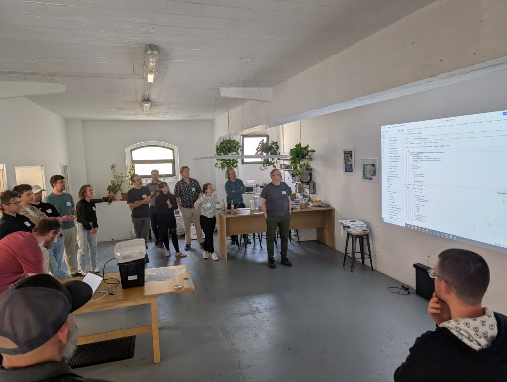 Photo of sprint attendees standing in a large circle around small text being projected on the wall. 